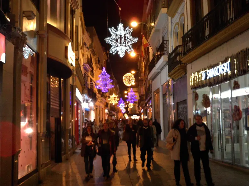 Calle Sierpes in Seville strung with warm Christmas lights as shoppers stroll below