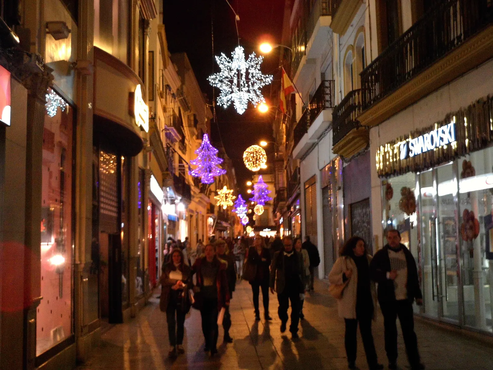 Calle Sierpes in Seville strung with warm Christmas lights as shoppers stroll below